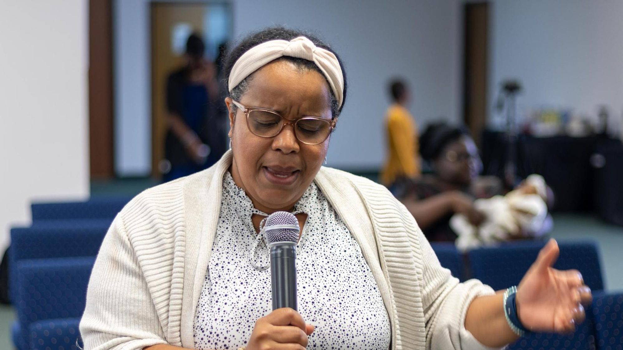 A woman leading the congregation in prayer with a microphone.
