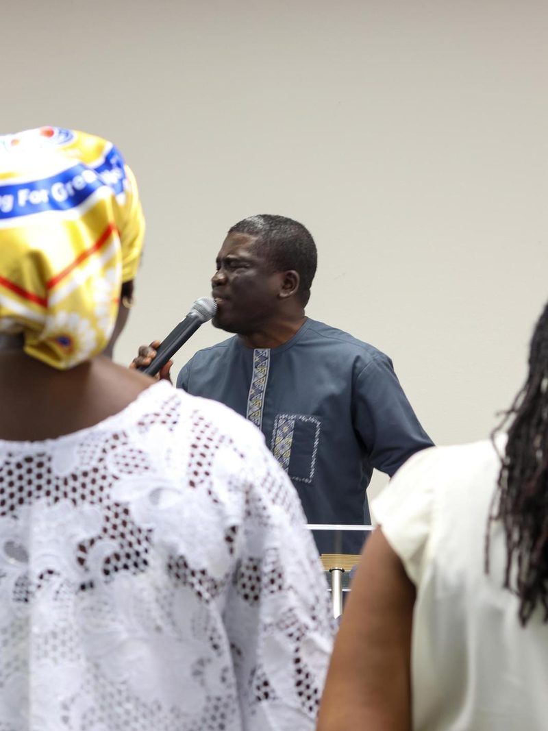A church leader praying over members of the congregation with a microphone in hand.