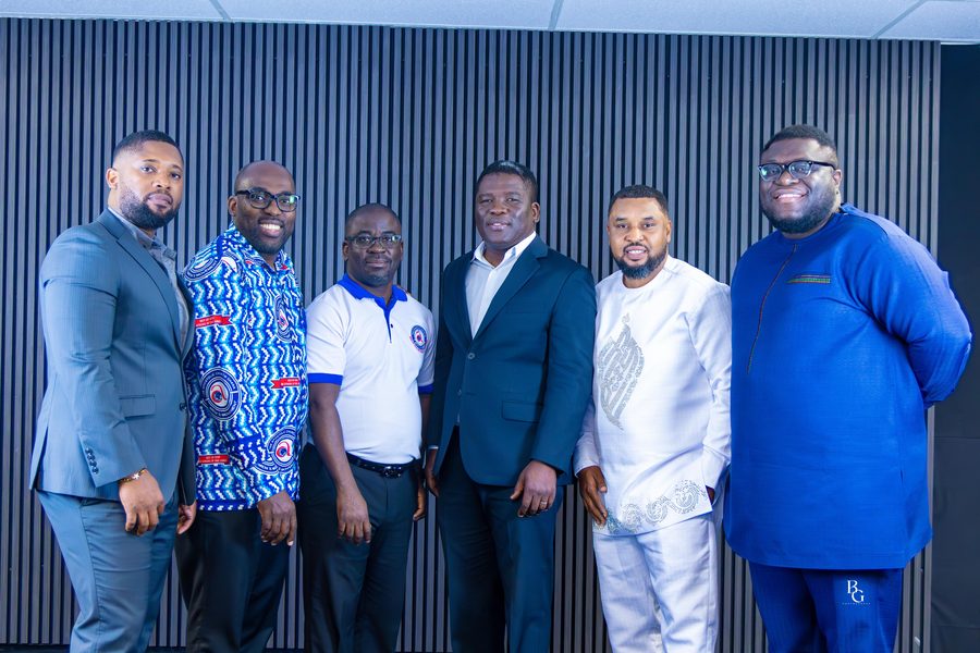 Six men of the assembly standing together at a Men&rsquo;s Movement gathering, two of them wearing Apostolic Church Men&rsquo;s Movement cloth.